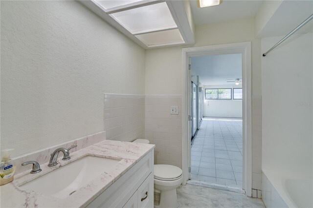 full bathroom featuring tile patterned floors, toilet, vanity, tile walls, and washtub / shower combination