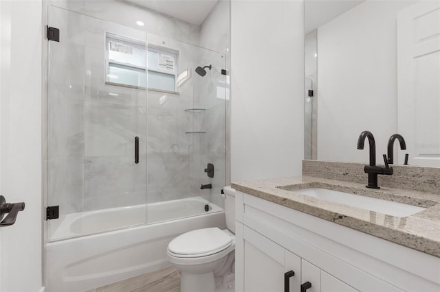 full bathroom with hardwood / wood-style floors, vanity, combined bath / shower with glass door, and toilet