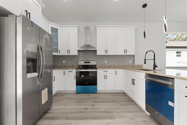 kitchen with appliances with stainless steel finishes, wall chimney exhaust hood, decorative light fixtures, light hardwood / wood-style flooring, and white cabinets