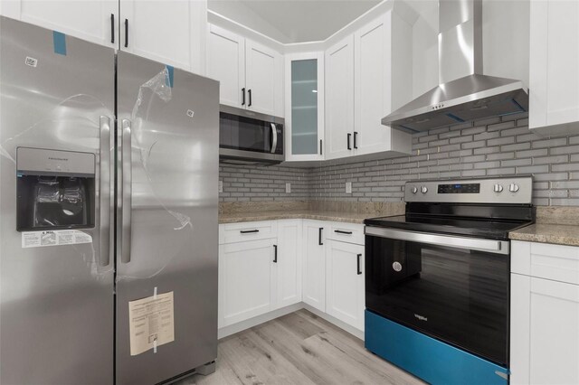 kitchen featuring white cabinetry, light wood-type flooring, appliances with stainless steel finishes, and wall chimney exhaust hood