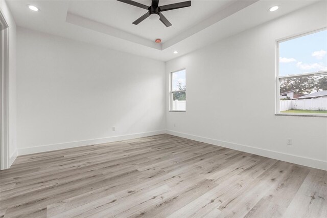 spare room with ceiling fan, a healthy amount of sunlight, light hardwood / wood-style flooring, and a tray ceiling