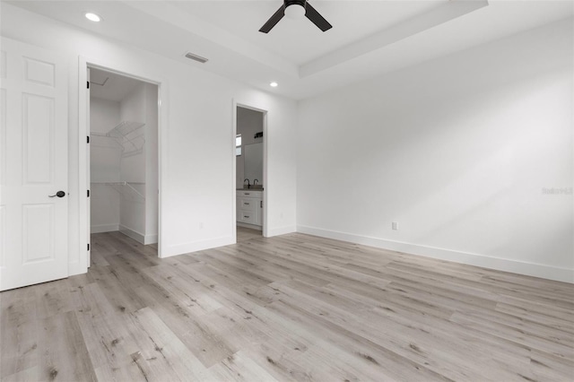 unfurnished bedroom featuring ceiling fan, a spacious closet, light hardwood / wood-style flooring, connected bathroom, and a closet