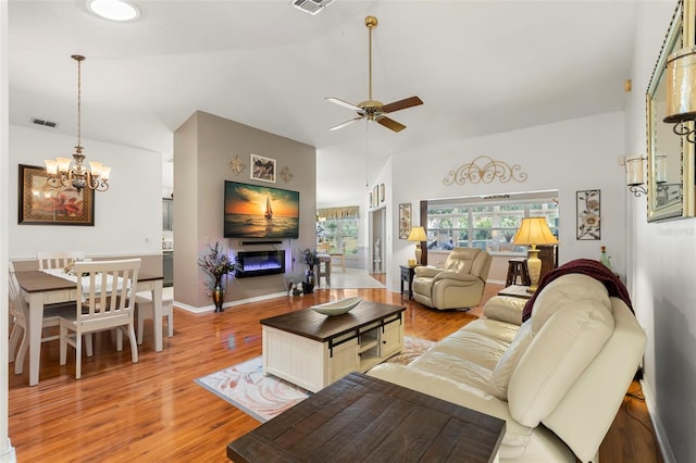 living room featuring lofted ceiling, ceiling fan with notable chandelier, and light wood-type flooring