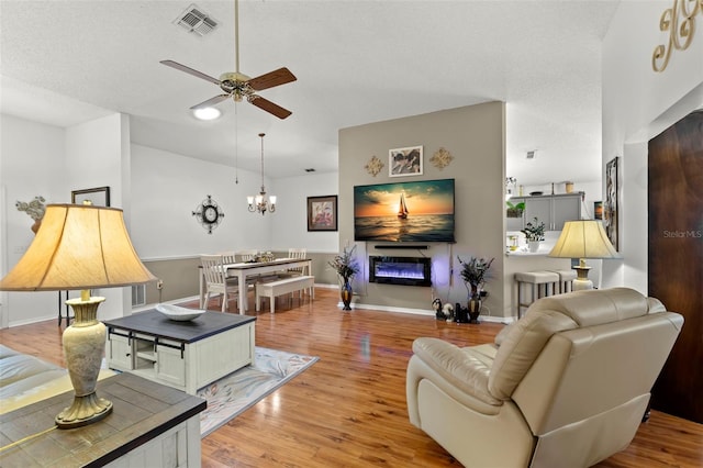 living room with ceiling fan with notable chandelier, a textured ceiling, and light wood-type flooring