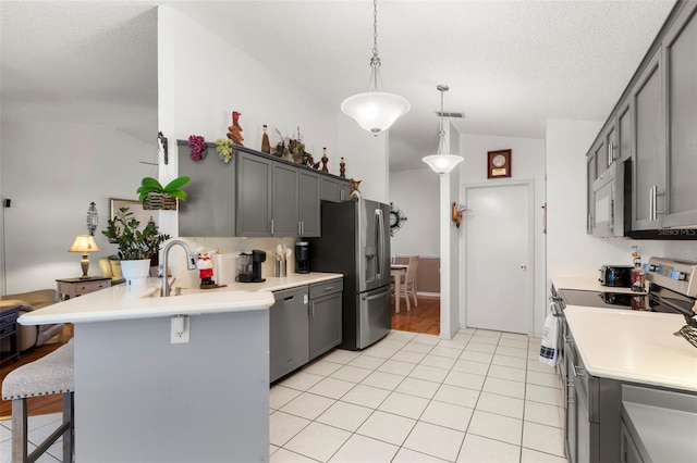 kitchen with a kitchen breakfast bar, kitchen peninsula, vaulted ceiling, pendant lighting, and appliances with stainless steel finishes