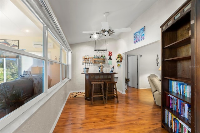 interior space featuring lofted ceiling, ceiling fan, hardwood / wood-style flooring, indoor bar, and an AC wall unit