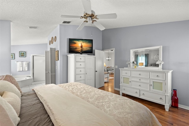 bedroom with wood-type flooring, vaulted ceiling, ensuite bathroom, a textured ceiling, and ceiling fan