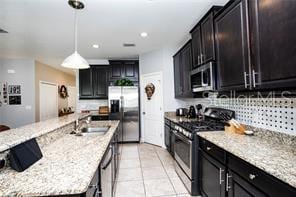 kitchen with light stone countertops, sink, stainless steel appliances, decorative light fixtures, and light tile patterned flooring