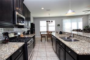 kitchen with light stone counters, sink, hanging light fixtures, and appliances with stainless steel finishes