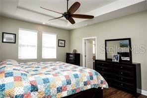 bedroom with a raised ceiling, ceiling fan, and dark wood-type flooring