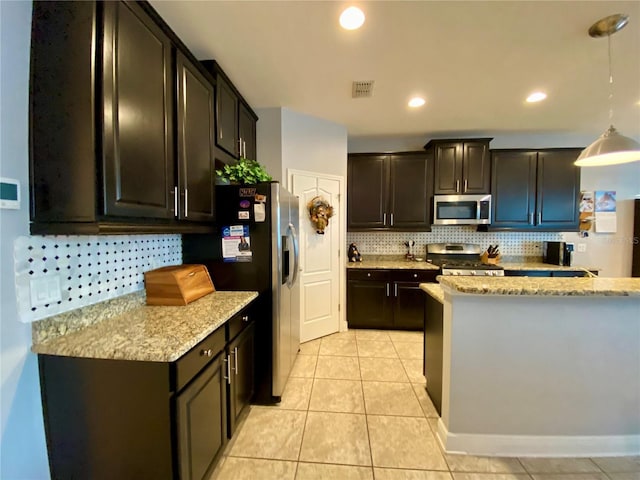 kitchen with light stone countertops, appliances with stainless steel finishes, tasteful backsplash, decorative light fixtures, and light tile patterned flooring