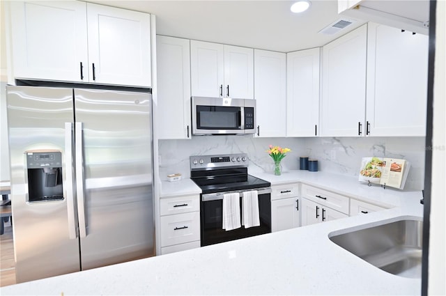 kitchen with appliances with stainless steel finishes, sink, backsplash, hardwood / wood-style floors, and white cabinets