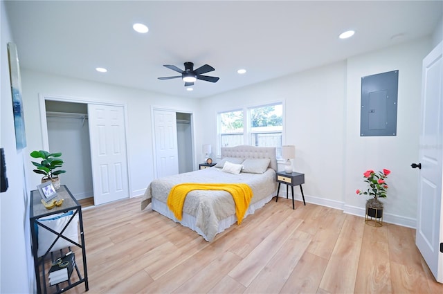 bedroom featuring electric panel, two closets, light hardwood / wood-style floors, and ceiling fan