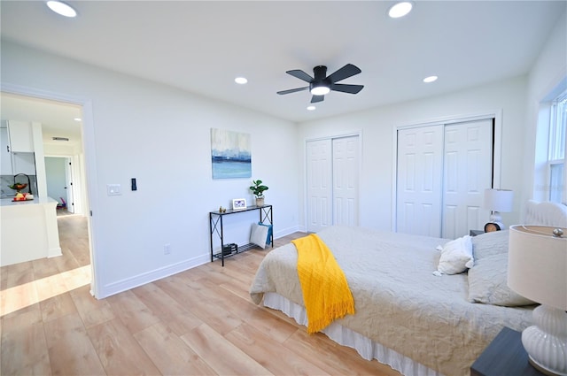 bedroom with ceiling fan, multiple closets, and light hardwood / wood-style flooring