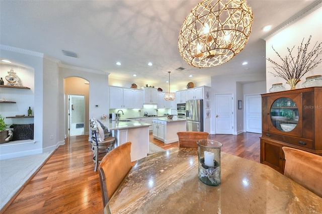 dining space featuring wood-type flooring, ornamental molding, sink, and an inviting chandelier