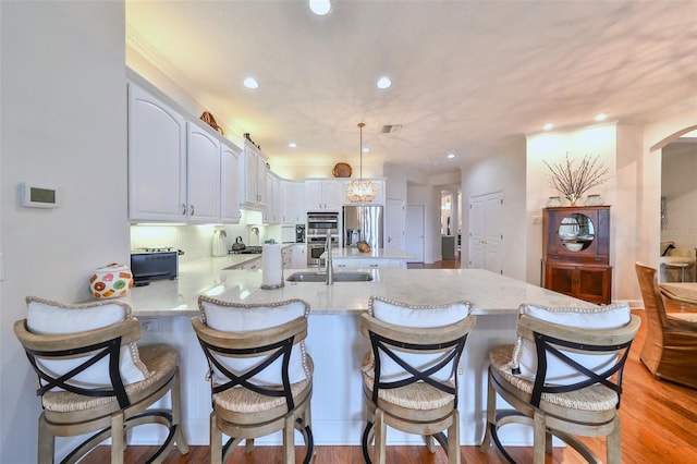 kitchen featuring kitchen peninsula, appliances with stainless steel finishes, a breakfast bar, white cabinetry, and hanging light fixtures