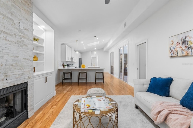 living room featuring built in shelves, light wood-type flooring, a stone fireplace, and sink