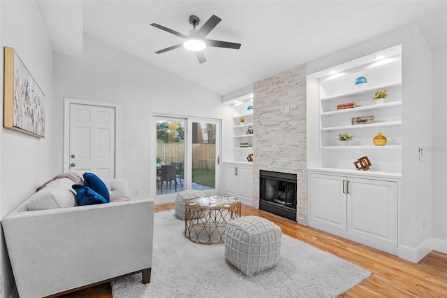 living room featuring a stone fireplace, vaulted ceiling, light hardwood / wood-style flooring, ceiling fan, and built in features