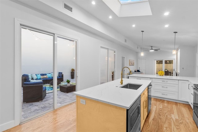 kitchen with vaulted ceiling with skylight, built in microwave, ceiling fan, sink, and an island with sink