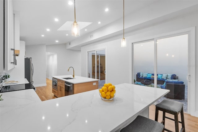 kitchen featuring light stone countertops, a kitchen island with sink, and hanging light fixtures