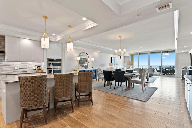 kitchen featuring stainless steel double oven, light stone counters, decorative light fixtures, and a tray ceiling