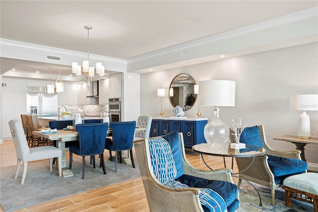 dining room with a notable chandelier, ornamental molding, and light wood-type flooring