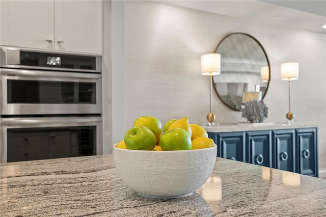 interior details featuring blue cabinetry, light stone countertops, and stainless steel double oven