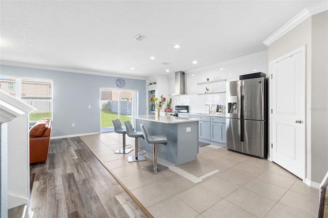 kitchen with wall chimney exhaust hood, a kitchen breakfast bar, appliances with stainless steel finishes, and crown molding