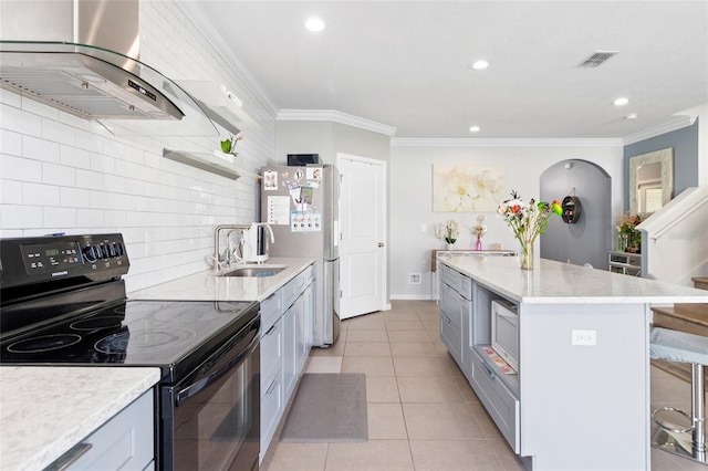 kitchen featuring a kitchen island, wall chimney range hood, backsplash, gray cabinets, and appliances with stainless steel finishes