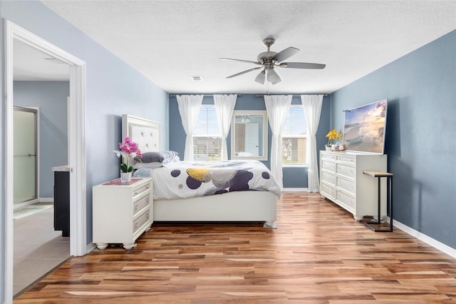 bedroom featuring ensuite bathroom, a textured ceiling, light hardwood / wood-style floors, and ceiling fan