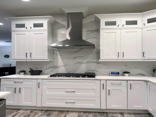 kitchen with tasteful backsplash, stainless steel appliances, wall chimney range hood, hardwood / wood-style flooring, and white cabinets