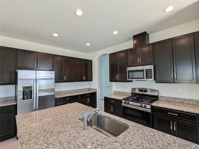 kitchen featuring dark brown cabinetry, light stone countertops, appliances with stainless steel finishes, and sink