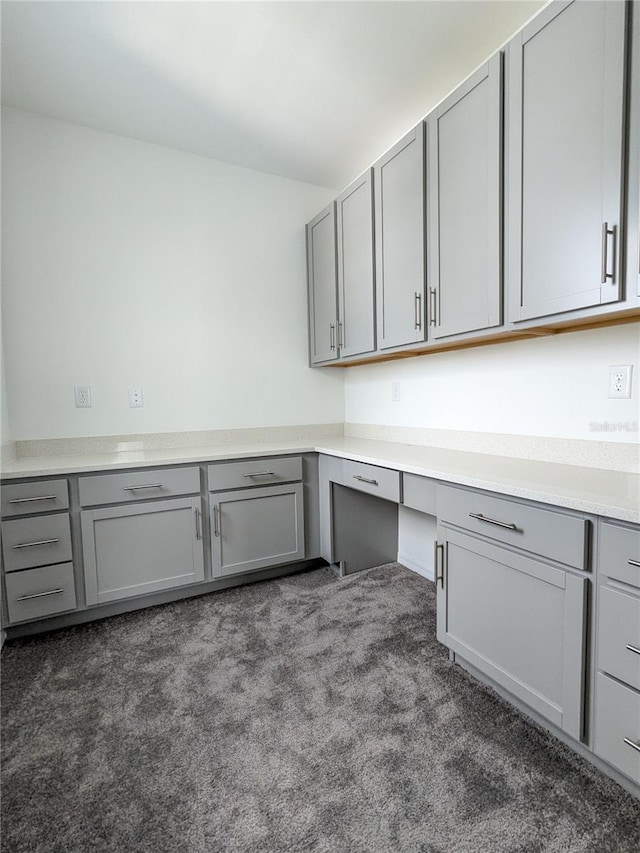 unfurnished office featuring built in desk and dark colored carpet