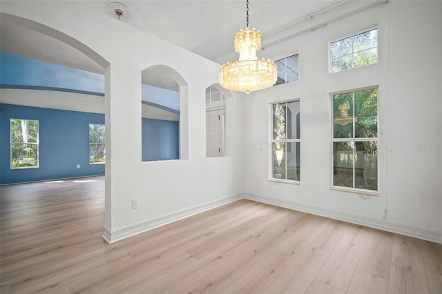 empty room with a chandelier, light hardwood / wood-style flooring, a towering ceiling, and a healthy amount of sunlight