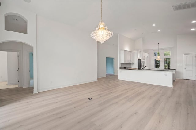 unfurnished living room with high vaulted ceiling, light hardwood / wood-style floors, and an inviting chandelier