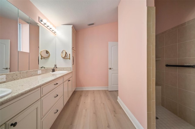 bathroom featuring hardwood / wood-style floors, vanity, a tile shower, and a textured ceiling