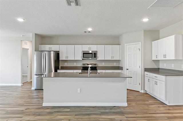 kitchen with hardwood / wood-style flooring, stainless steel appliances, a kitchen island with sink, and white cabinets