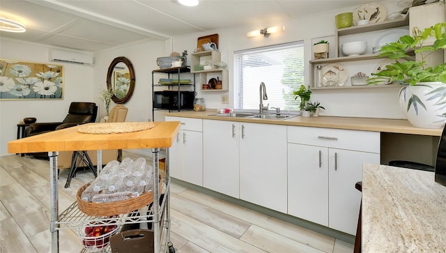 kitchen featuring white cabinetry, light hardwood / wood-style flooring, butcher block counters, an AC wall unit, and sink