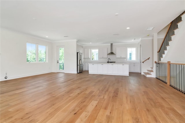 unfurnished living room featuring crown molding, light wood-type flooring, stairs, a sink, and recessed lighting