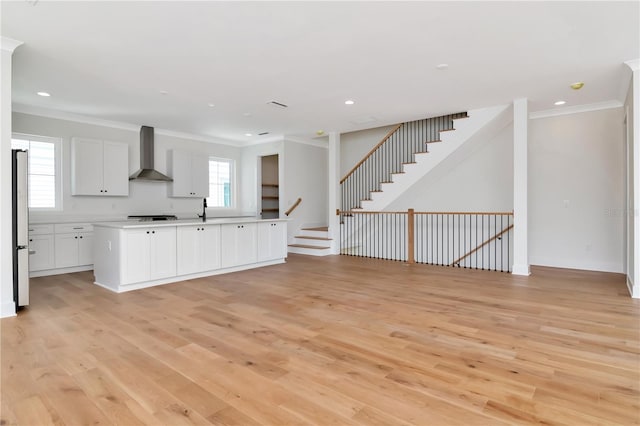 kitchen with ornamental molding, open floor plan, wall chimney exhaust hood, light wood-style flooring, and appliances with stainless steel finishes