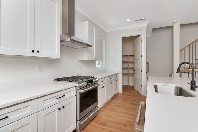 kitchen featuring a sink, wall chimney exhaust hood, gas range, and white cabinetry