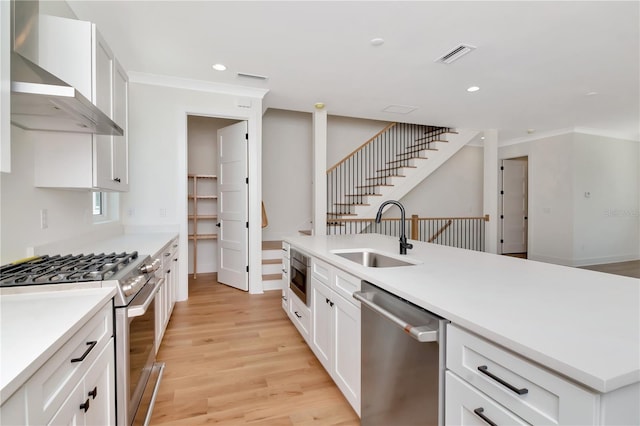 kitchen with appliances with stainless steel finishes, a sink, light wood-style floors, wall chimney exhaust hood, and recessed lighting