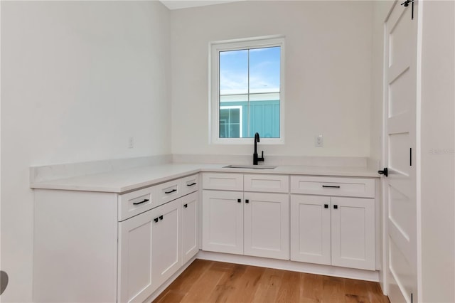 kitchen with a sink, light countertops, light wood finished floors, and white cabinetry
