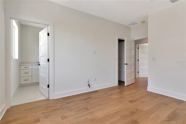 unfurnished bedroom with connected bathroom, baseboards, and light wood-style flooring