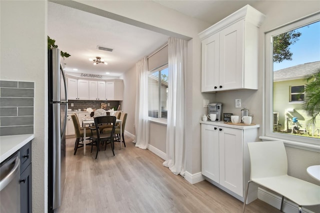 kitchen featuring decorative backsplash, stainless steel appliances, white cabinets, and light wood-type flooring