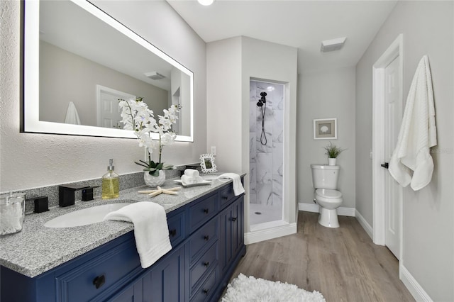 bathroom with hardwood / wood-style flooring, vanity, toilet, and a tile shower