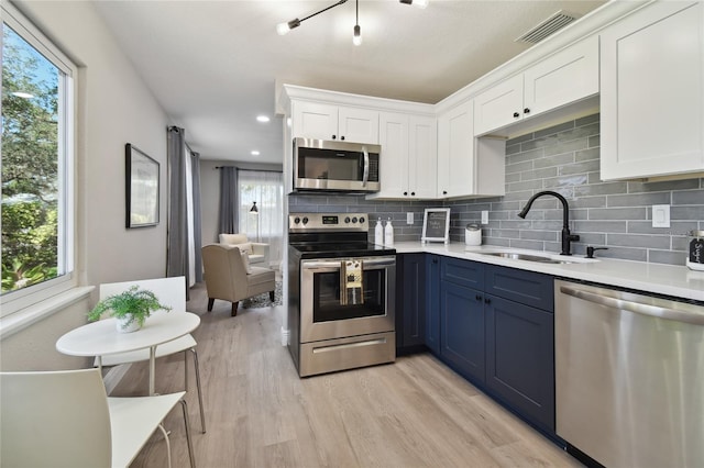 kitchen with sink, blue cabinetry, stainless steel appliances, light hardwood / wood-style floors, and white cabinets