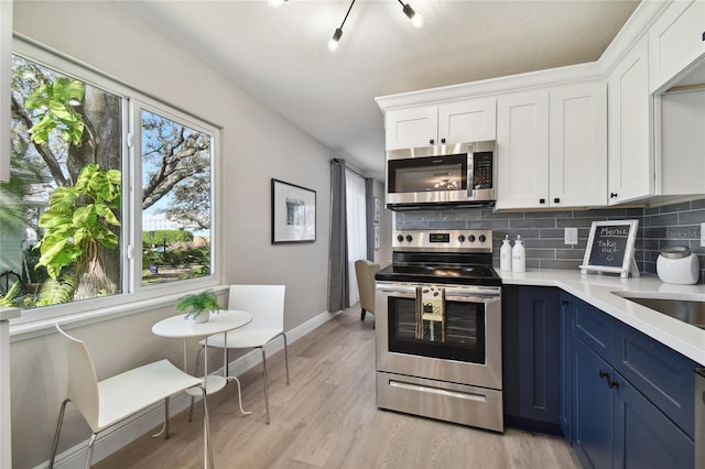 kitchen featuring tasteful backsplash, white cabinets, stainless steel appliances, plenty of natural light, and blue cabinetry