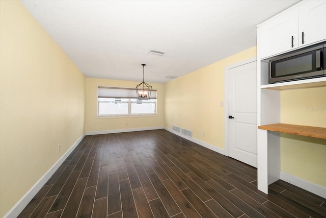 unfurnished dining area featuring dark wood-type flooring, built in desk, and a chandelier