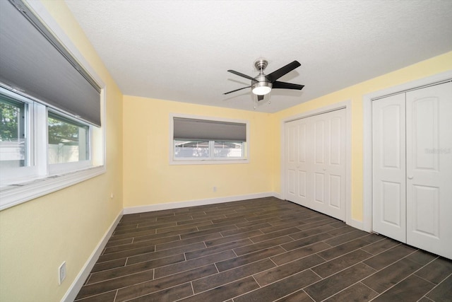 unfurnished bedroom featuring dark wood-type flooring, two closets, a textured ceiling, and ceiling fan